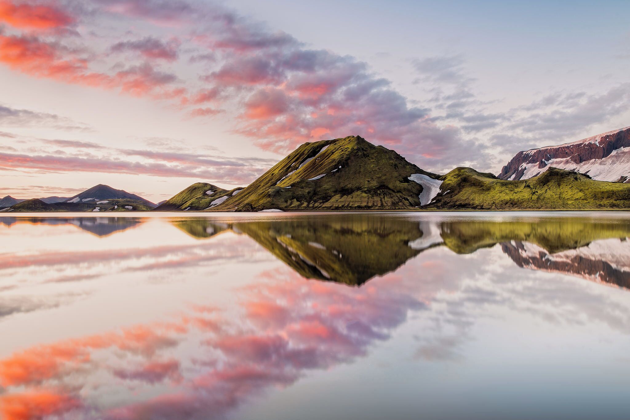 Ein Bergmassiv mit Schneeflecken und ein ruhiger See, der den Himmel spiegelt.