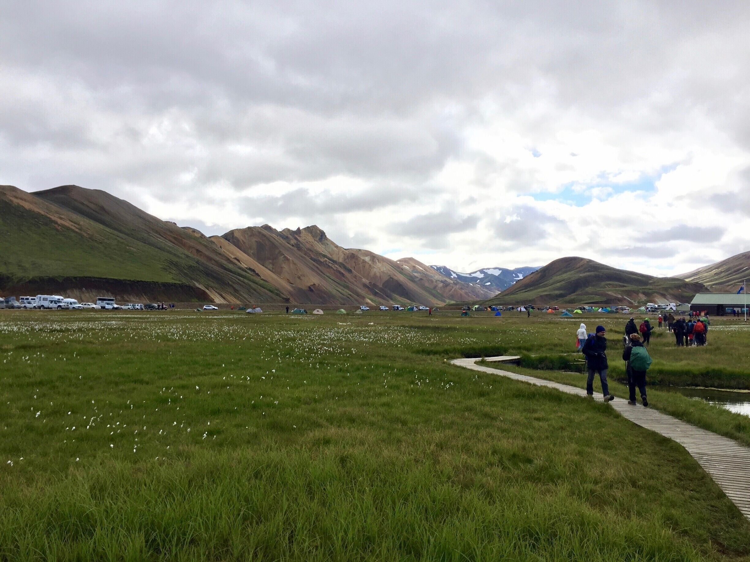 A grassy field with tents and vehicles, surrounded by mountains.
