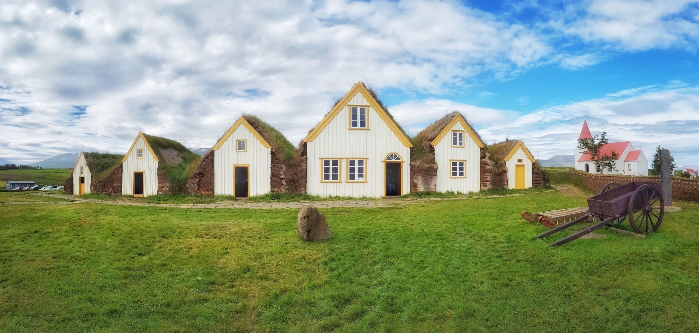 A row of white houses with yellow trim and grass-covered roofs, set against a cloudy sky.