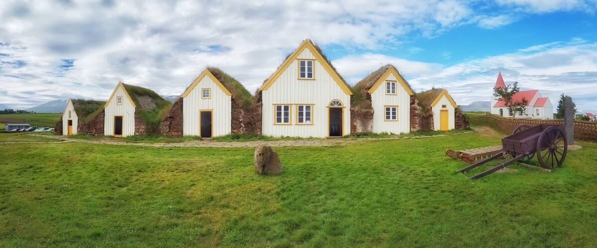A row of white houses with yellow trim and grass-covered roofs, set against a cloudy sky.
