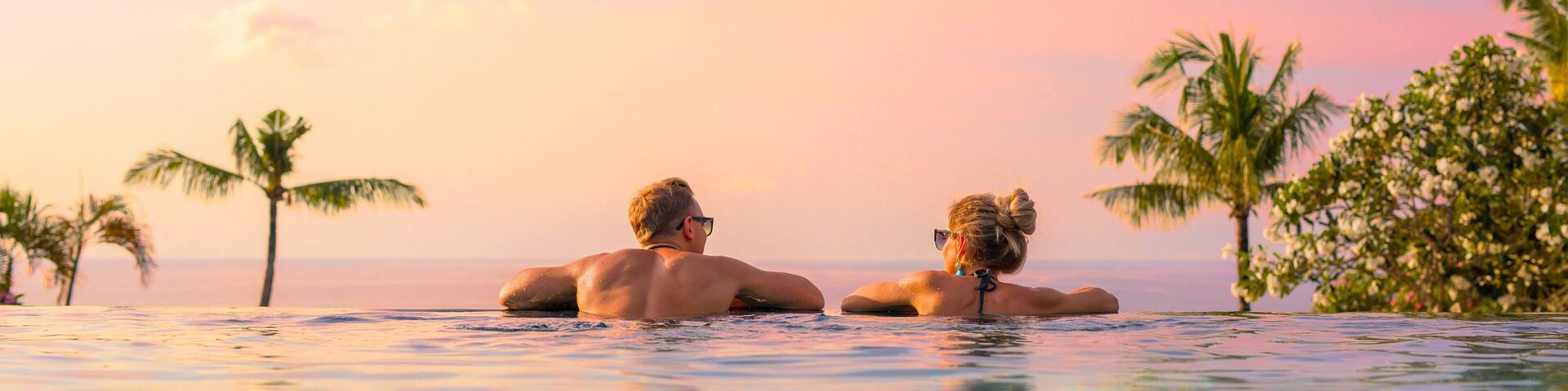 Panoramic photo of couple in pool enjoying tropical vacation by sunset