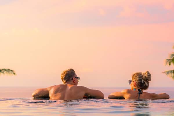 Panoramic photo of couple in pool enjoying tropical vacation by sunset