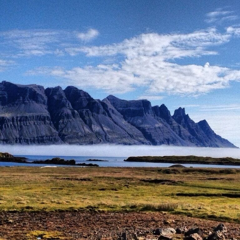 A mountainous landscape with a grassy foreground and a body of water in the distance.