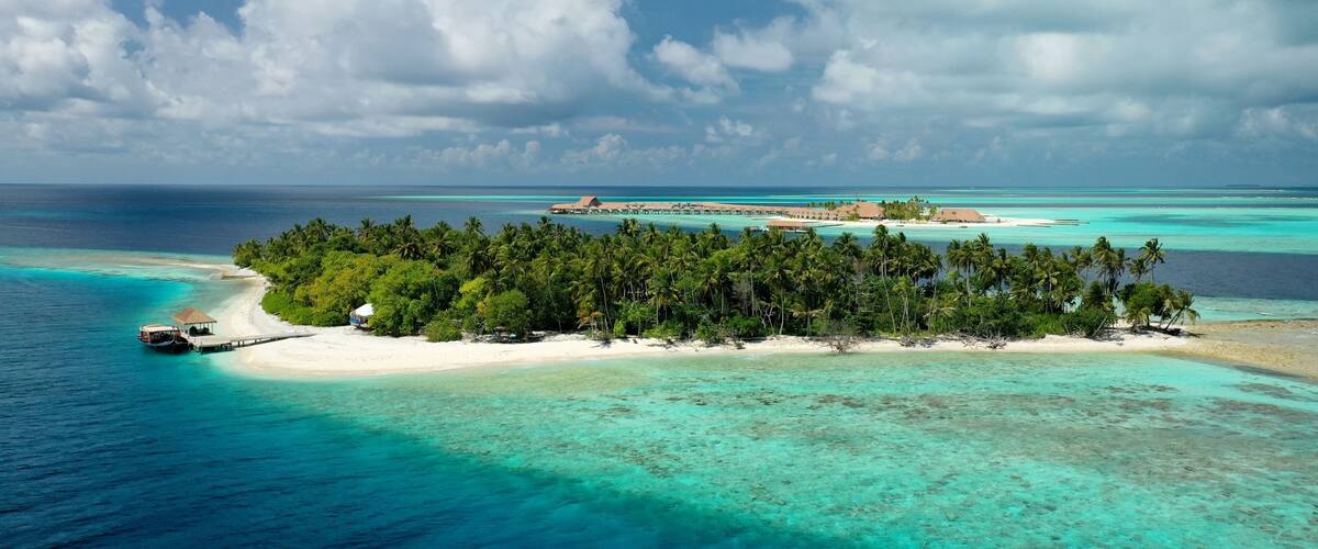 A tropical island with a white sandy beach, dense palm trees, clear turquoise waters, and a small boat docked on the shore.