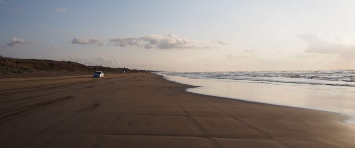 A beach with a sandy shore, a few cars parked, and a clear sky.