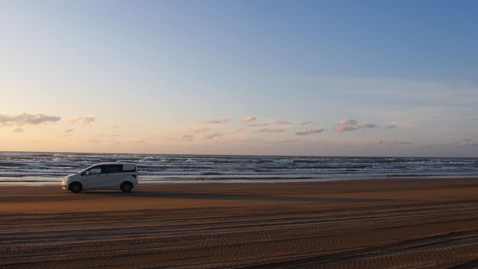 A white car parked on a sandy beach with the ocean in the background.