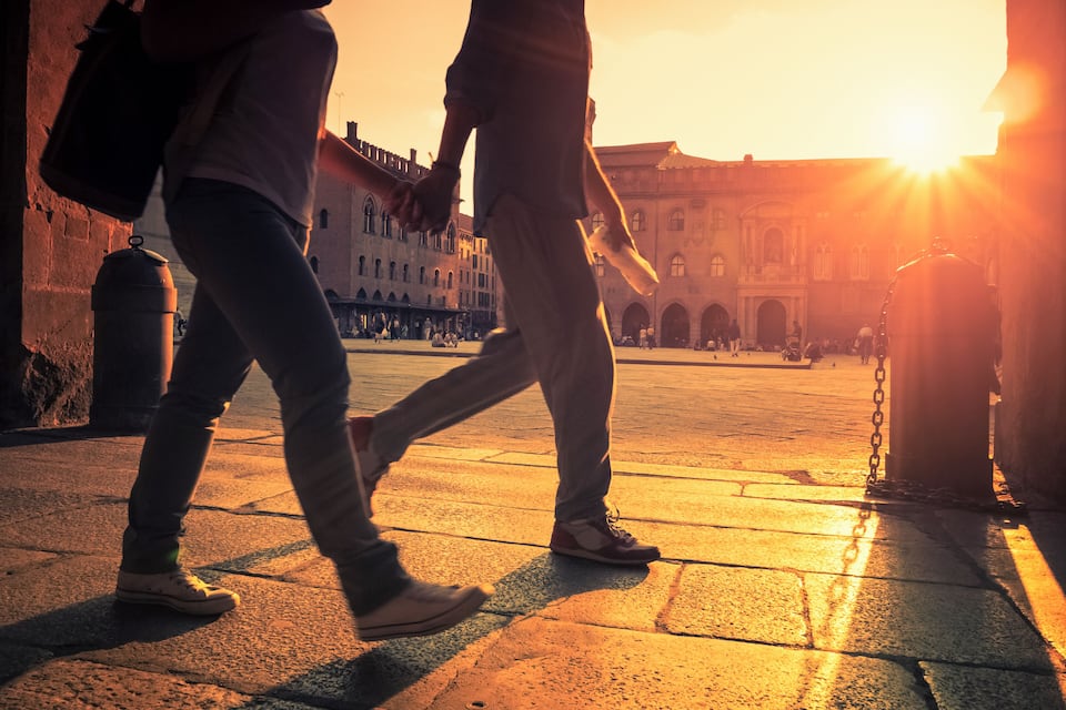Two people walking on a cobblestone street with a sunset in the background.
