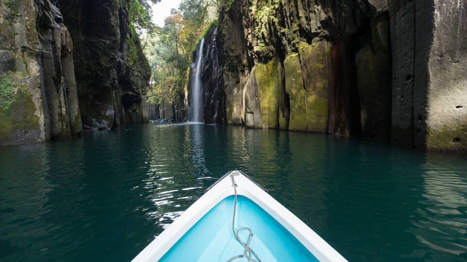 A boat in a narrow waterway flanked by rocky cliffs and a waterfall.