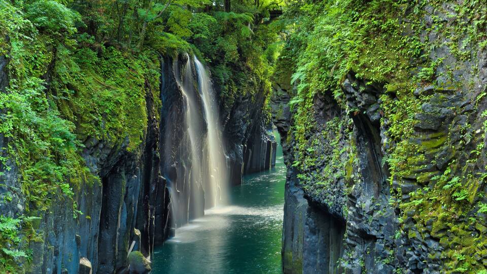A waterfall cascading down a rocky gorge surrounded by lush green vegetation.