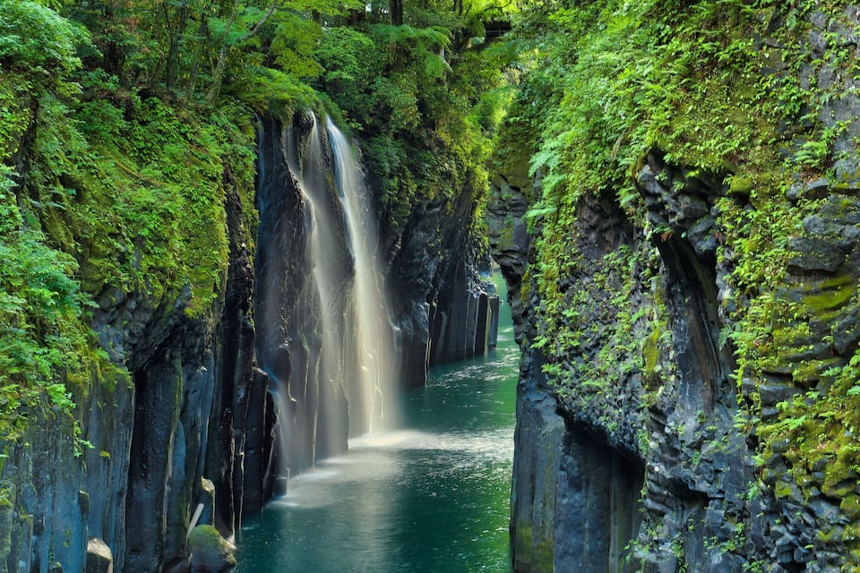 Una cascada se precipita por un desfiladero rocoso rodeado de exuberante vegetación verde.