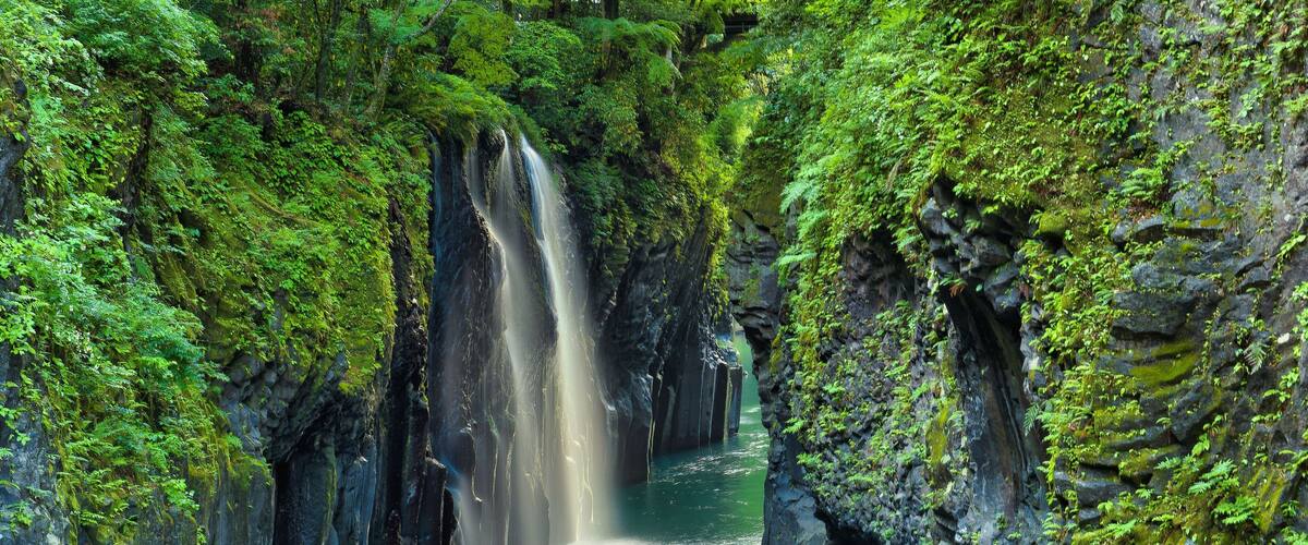 A waterfall cascading down a rocky gorge surrounded by lush green vegetation.