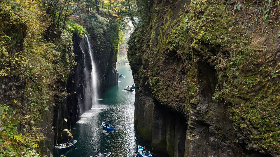 A narrow canyon with a waterfall, surrounded by dense foliage and rocky cliffs.