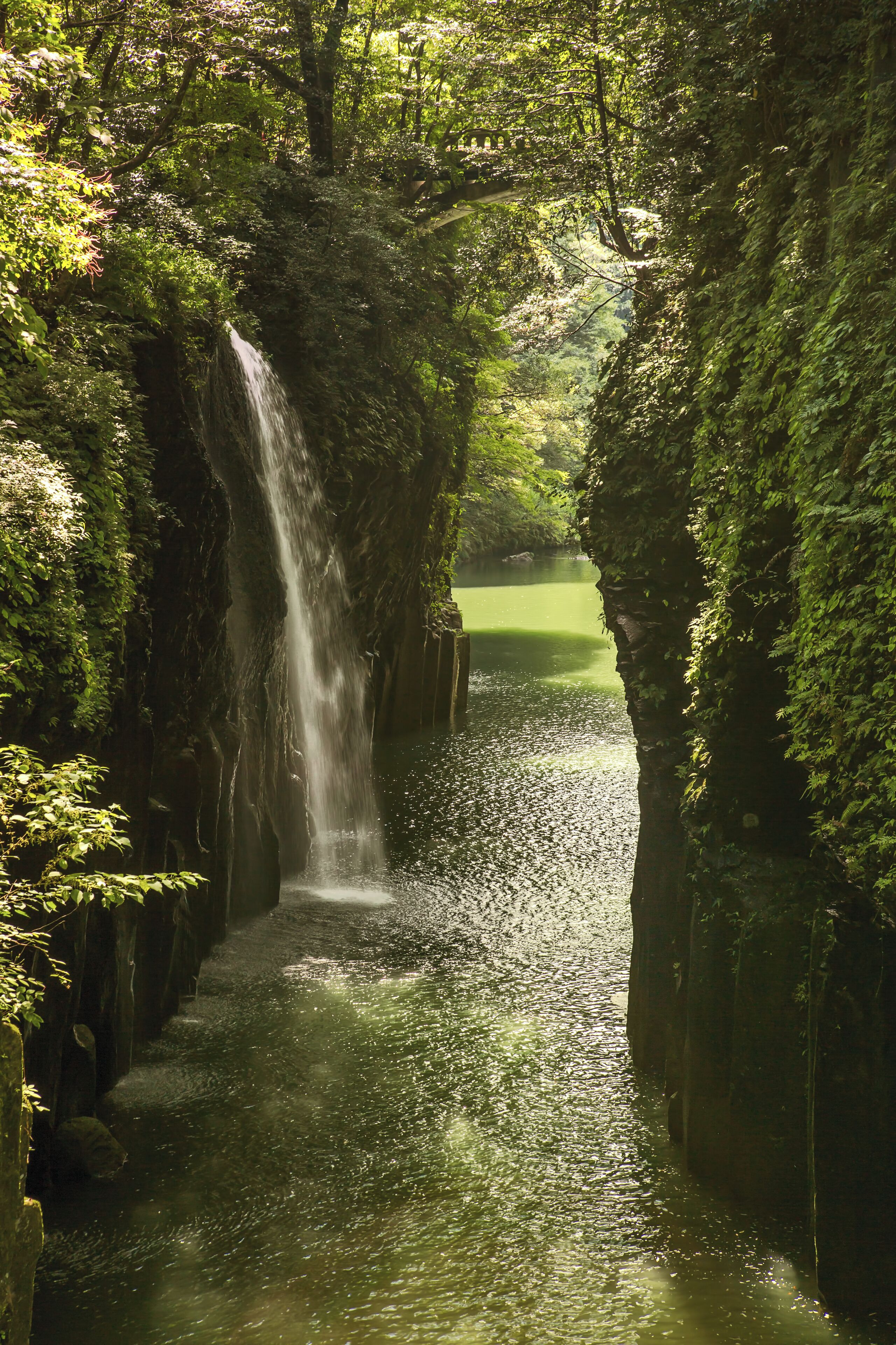 Takachiho Gorge (高千穂峡, Takachiho-kyō) is a narrow chasm cut through the rock by the Gokase River. Volcanic basalt columns line the sheer cliffs of the gorge, originally as a result of Mt. Aso’s eruption and further shaped through time by the flowing river, creating interesting shapes and patterns.
.
The 17-meter Manai Falls is probably the highlight of the tour, as it cascades into the river below and along with the gorge and the bridge makes for a very picturesque location. Normally, boat rides are offered to visitors but during the day of our visit it was temporarily stopped due to the high waters brought about by the recent typhoon.