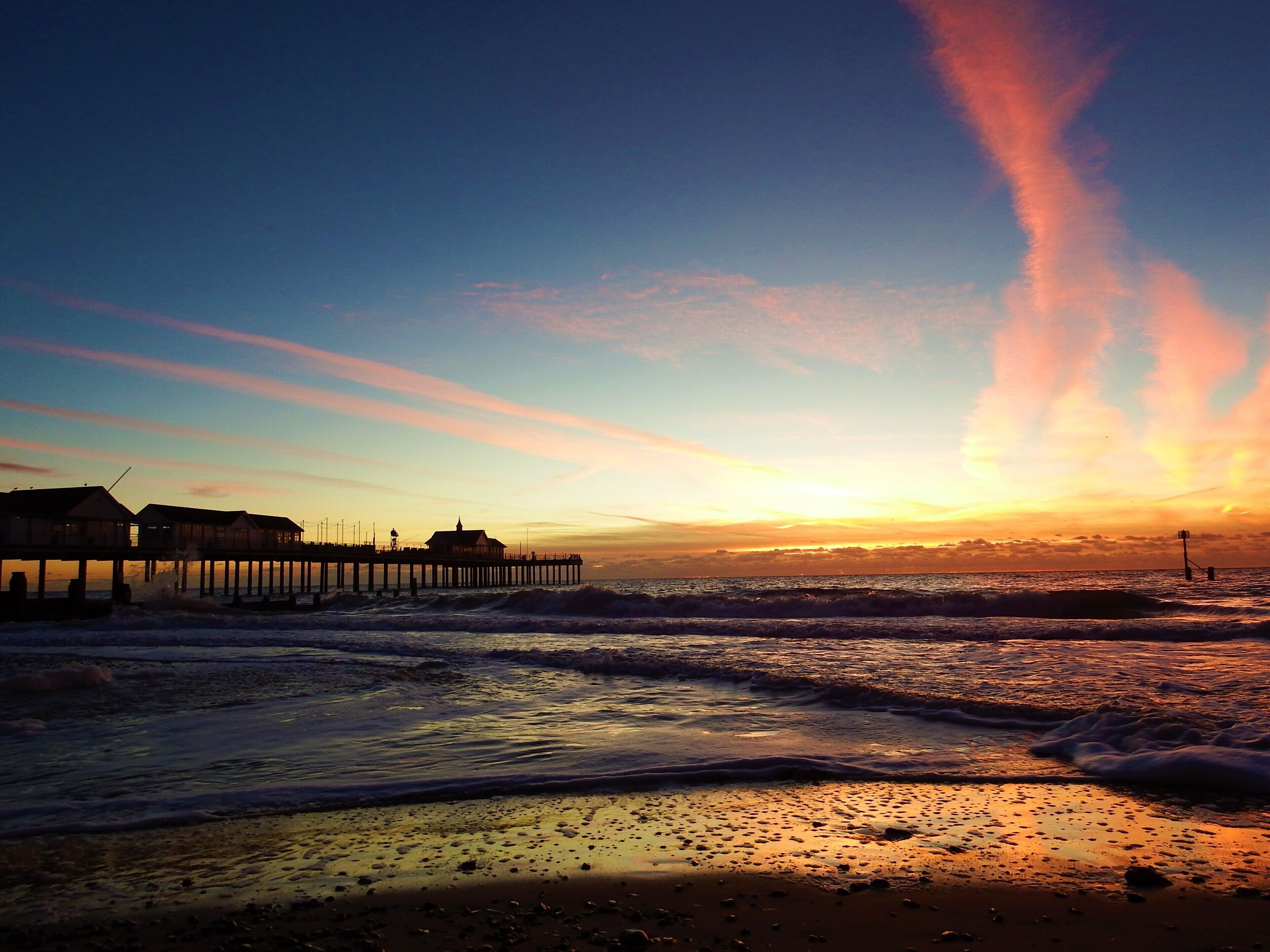 A pier extending into the ocean at sunset with waves crashing onto the shore.