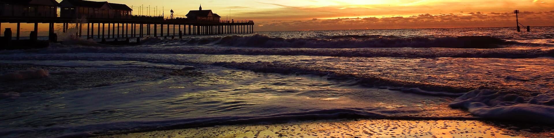 A pier extending into the ocean at sunset with waves crashing onto the shore.