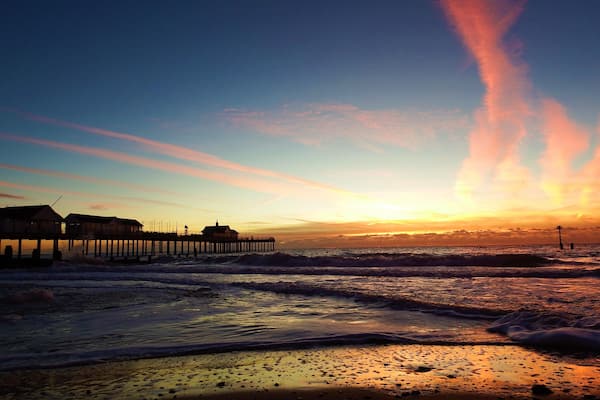 A pier extending into the ocean at sunset with waves crashing onto the shore.