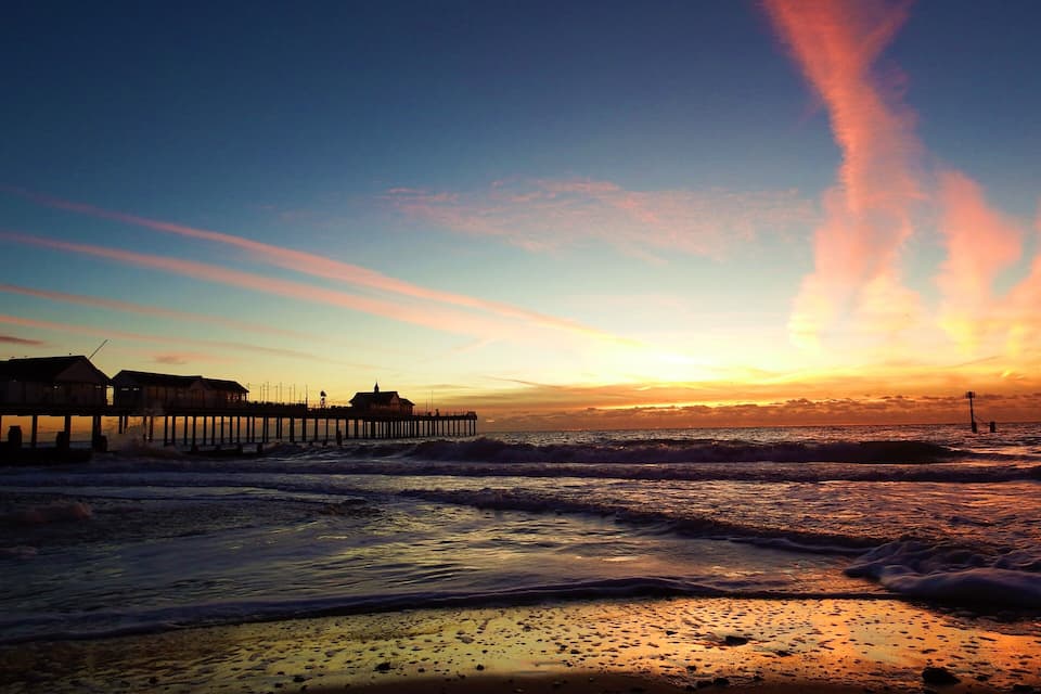 A pier extending into the ocean at sunset with waves crashing onto the shore.