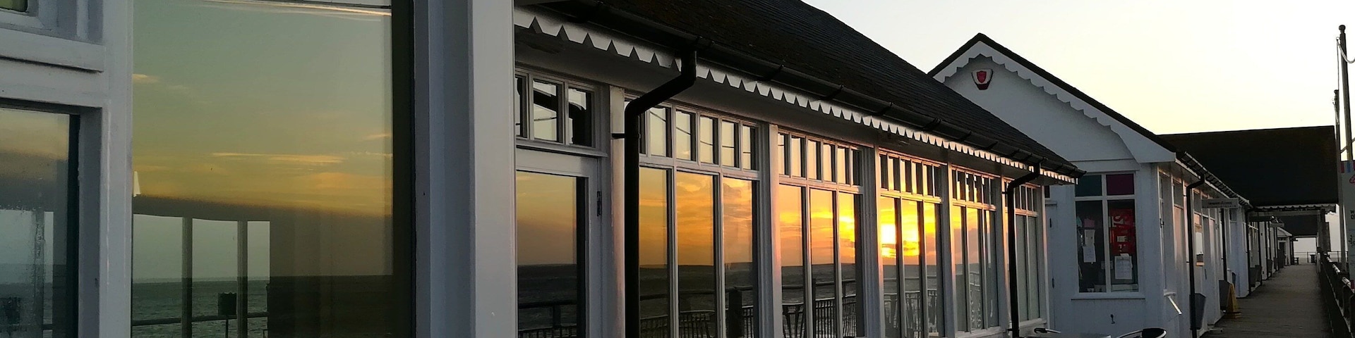 Restaurante à beira-mar com mesas ao ar livre e amplas janelas com vista para o oceano.