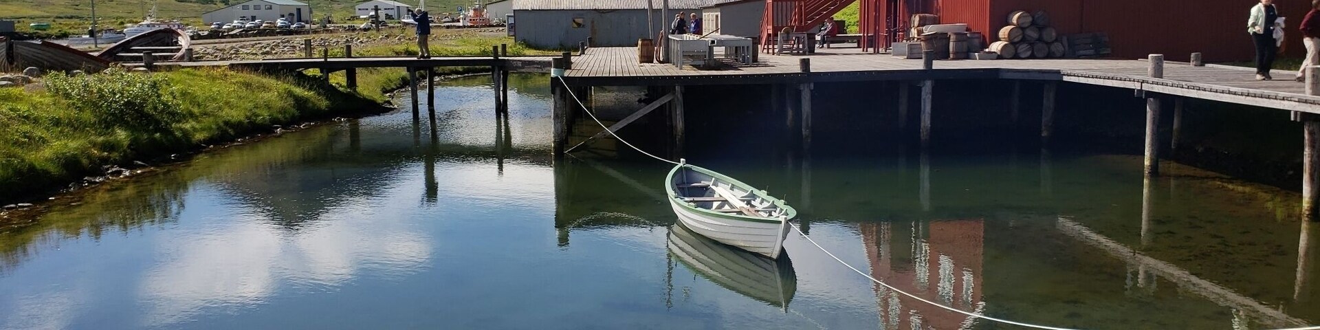 A calm river with a small boat tied to a dock, a red building, and a mountain in the background.