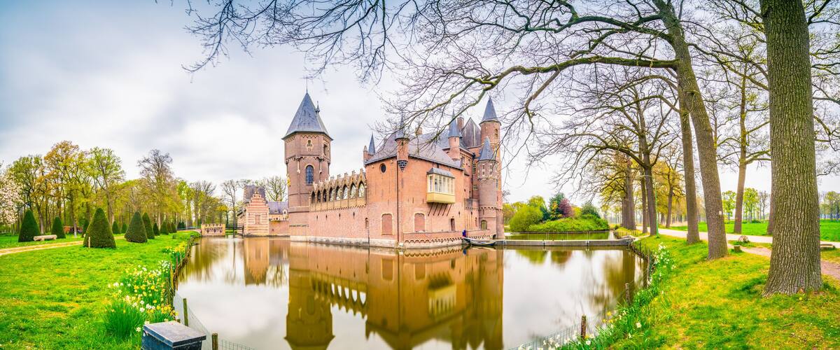 A historic castle with a moat, surrounded by lush greenery and trees.