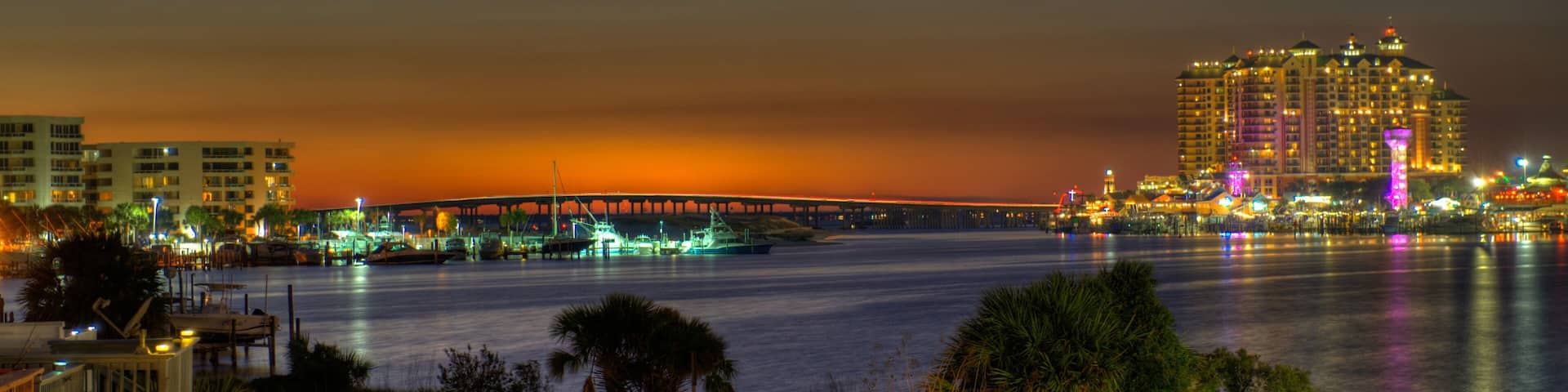 A cityscape at night with a bridge, waterfront buildings, and boats.
