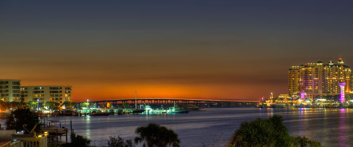 A cityscape at night with a bridge, waterfront buildings, and boats.