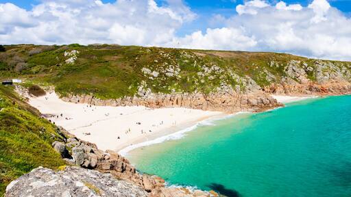 A coastal landscape with a sandy beach, clear turquoise waters, and rocky cliffs.