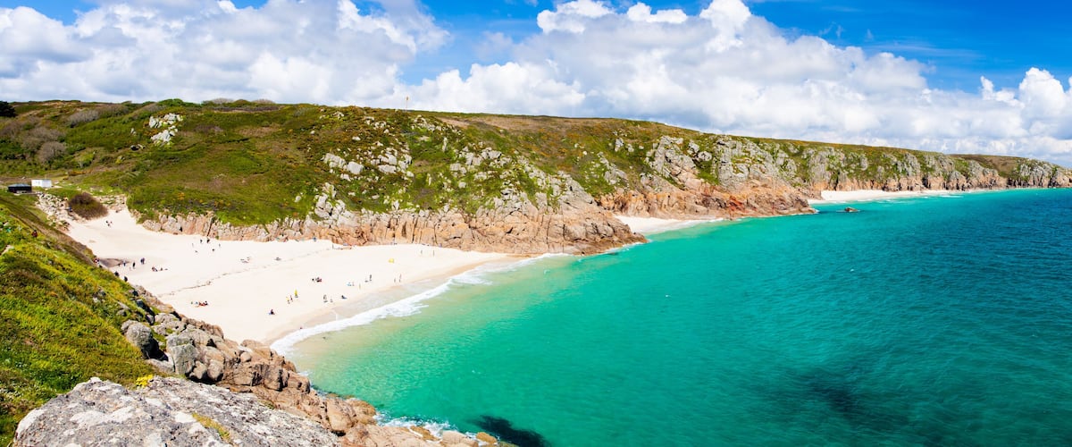 A coastal landscape with a sandy beach, clear turquoise waters, and rocky cliffs.
