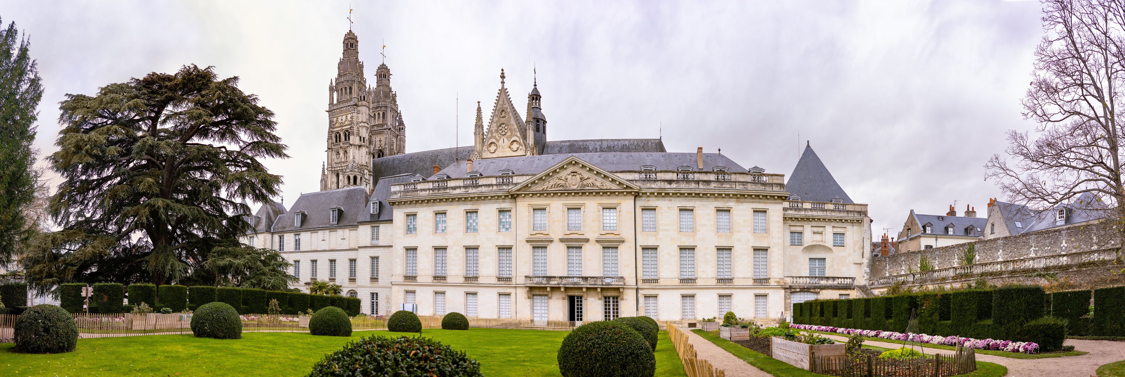 A large, historic building with a central courtyard, surrounded by well-manicured gardens and tall trees.