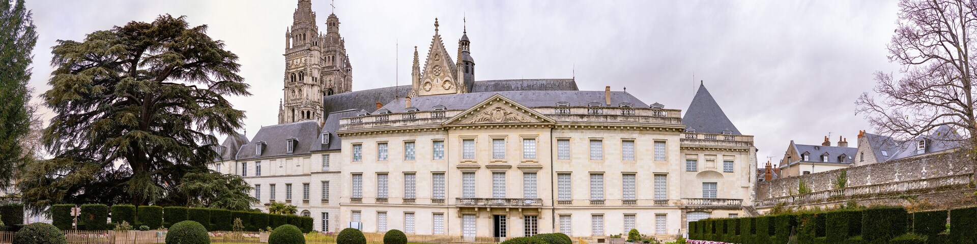 A large, historic building with a central courtyard, surrounded by well-manicured gardens and tall trees.