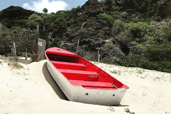 Un bateau rouge sur une plage de sable, avec une colline rocheuse en arrière-plan.