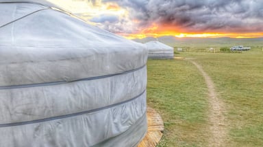 Eine Jurte in einem grasbewachsen Feld, im Hintergrund ein Sonnenuntergang.