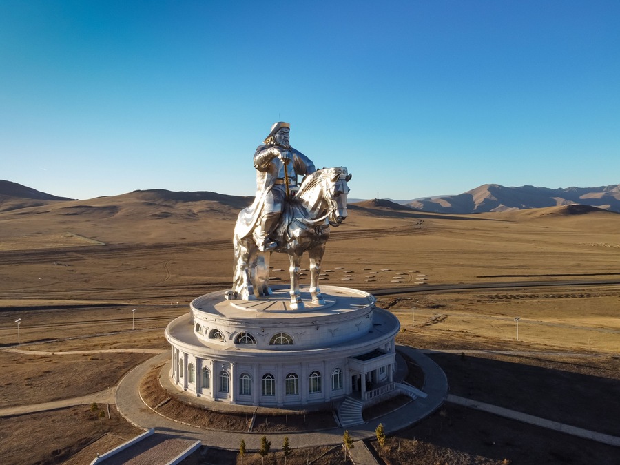 A statue of a mounted figure on a circular pedestal with a clear sky and distant mountains in the background.