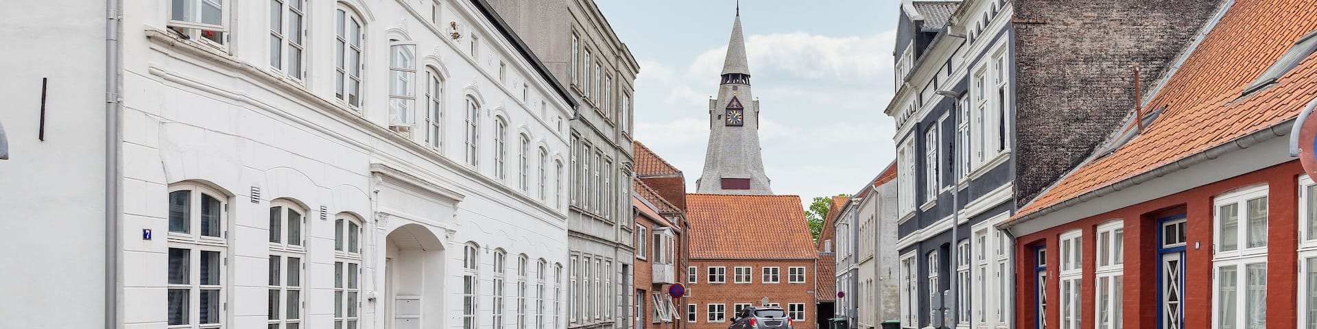 A street with white and red buildings, a church steeple, and a clear sky.