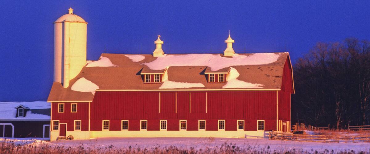 A red barn with a silo and a snow-covered landscape.