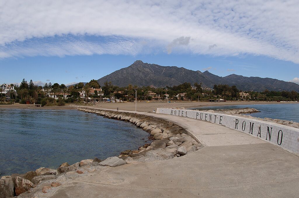 A coastal area with Hotel Punta Romano, a beach, and a mountain in the background.