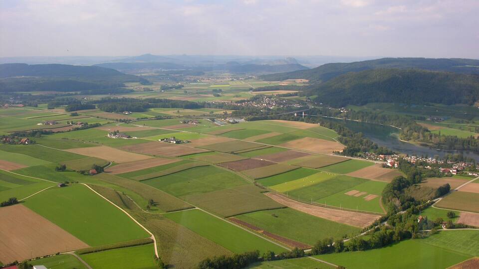 A rural landscape with fields, a river, and scattered houses.