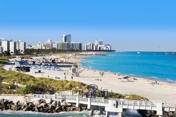 A coastal cityscape with a beach, a bridge, and a clear blue sky.