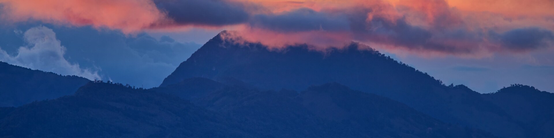 A view of the Costa Rican volcano in the clouds, lit by the setting sun. Quetzal forest after sunset. Los Quetzales National Park Nature Reserve. Costa rica.