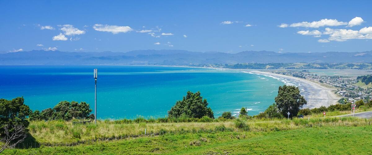 A coastal landscape with a clear blue sea, a sandy beach, and a road leading to a small town.