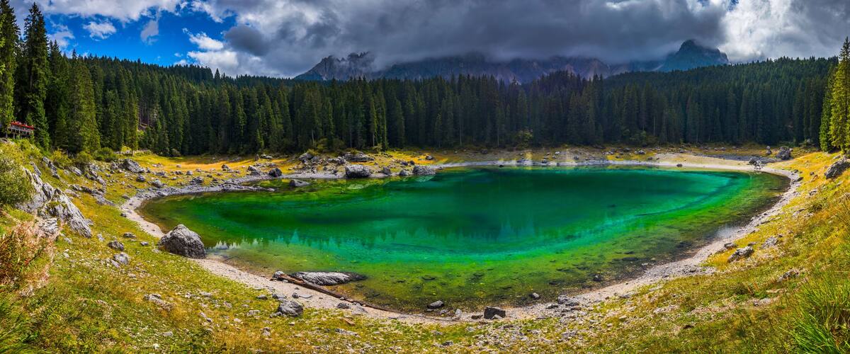 A turquoise lake surrounded by dense forest and mountains under a cloudy sky.