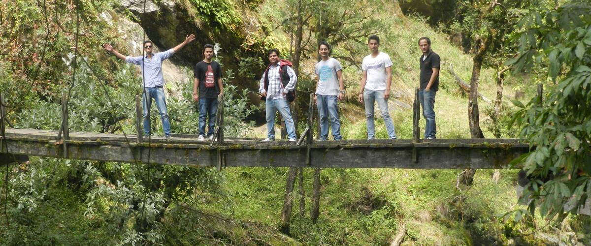 A group of people standing on a wooden bridge over a flowing river surrounded by lush greenery.
