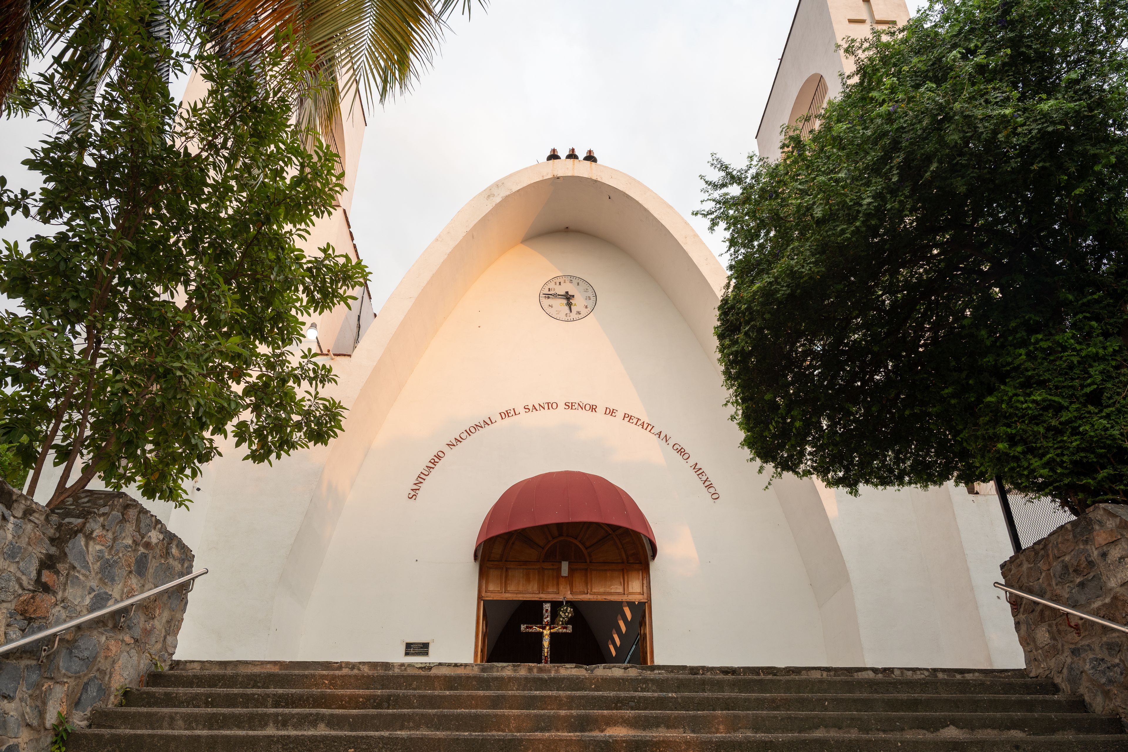 Eingang einer Kirche mit einer Uhr, Stufen und einem Schild mit der Aufschrift 'Santo Señor de Petatlán, Gro, Mexiko'.