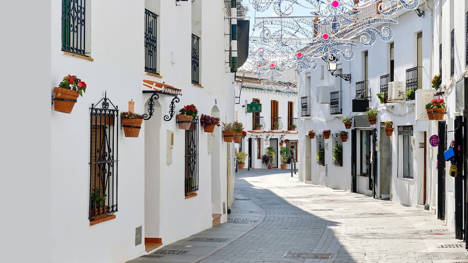 Panoramic image white copy space view, empty street famous village of Mijas in Spain. Charming narrow streets with New Year decorations, hanging flower pots on walls, no people. Costa del Sol, Malaga