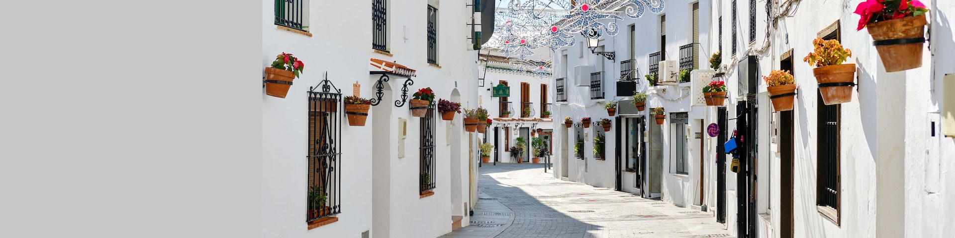 Panoramic image white copy space view, empty street famous village of Mijas in Spain. Charming narrow streets with New Year decorations, hanging flower pots on walls, no people. Costa del Sol, Malaga