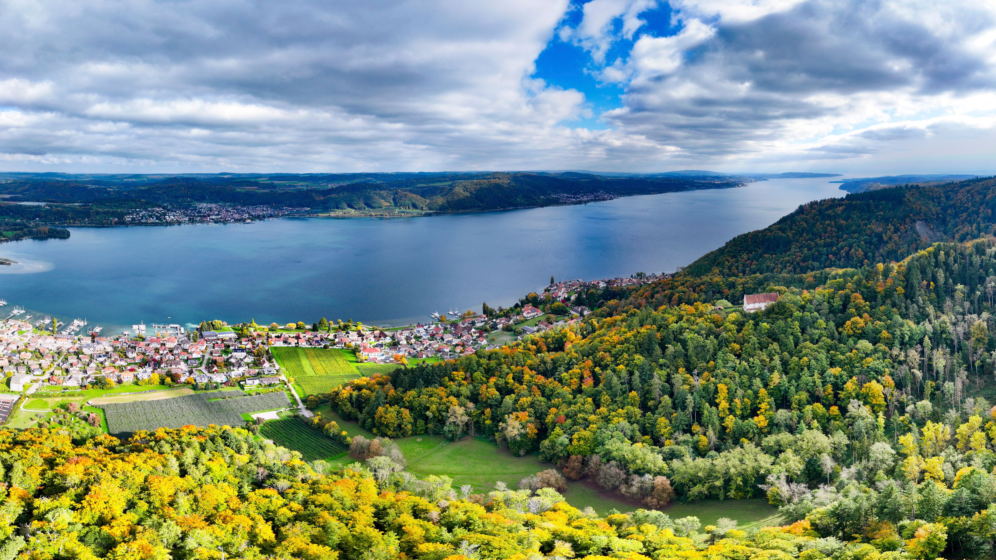 A detailed aerial panorama of Lake Constance in Switzerland, captured with a drone and showcasing a peaceful lakeside village surrounded by natural beauty. 