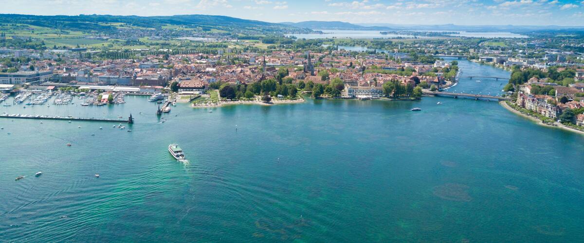 Une rivière traverse une ville, on y voit des bateaux, un pont et, au loin, des montagnes.