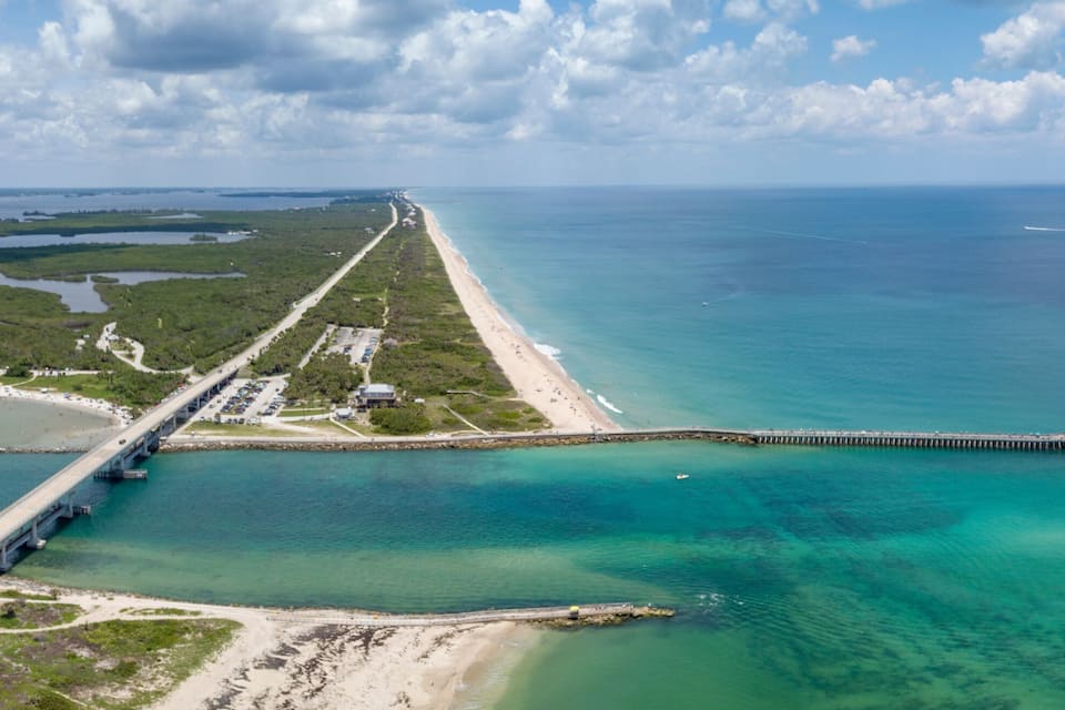 A coastal bridge connecting two landmasses, a beach, and a clear blue sea.