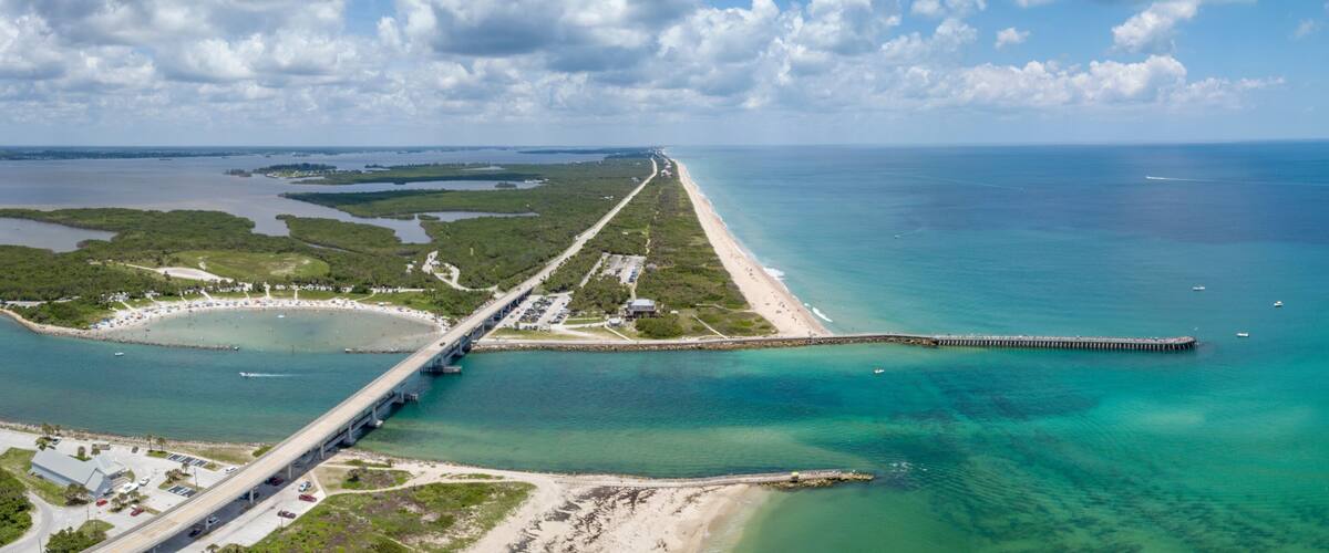 A coastal bridge connecting two landmasses, a beach, and a clear blue sea.
