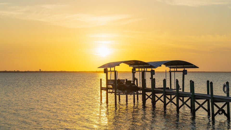 View of a sunset over a wooden pier in Indian River, Florida from the A1A. Wooden pillars of the old pier near the coast as a typical view of Florida